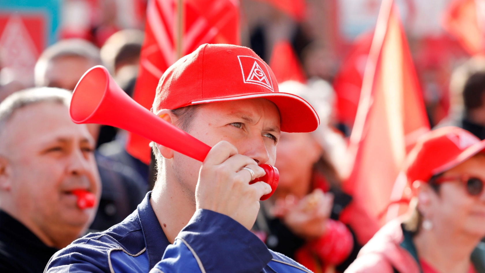Ein Mann mit IG Metall-Kappe und Signaltröte in einer Menschenmenge