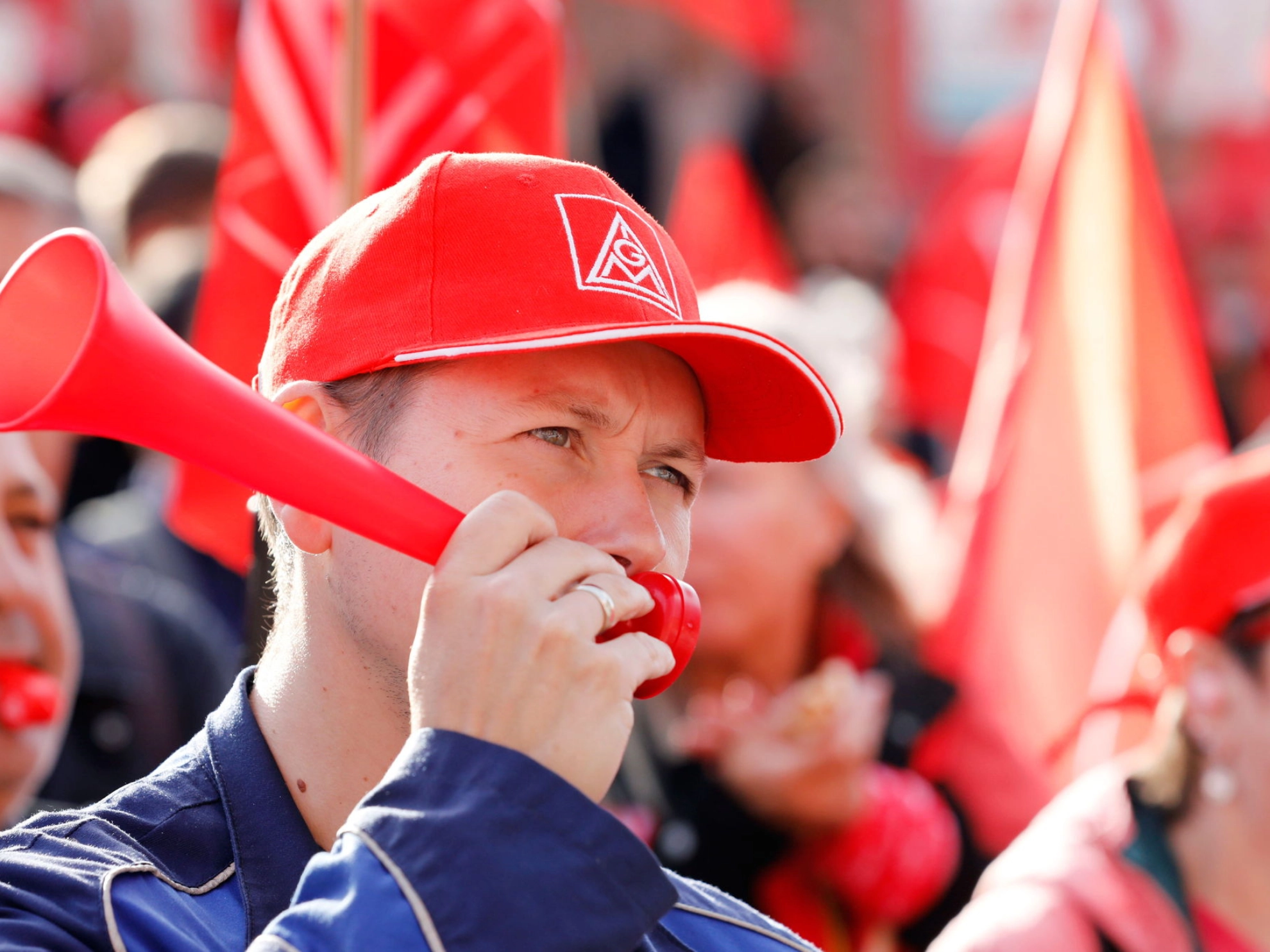 Ein Mann mit IG Metall-Kappe und Signaltröte in einer Menschenmenge