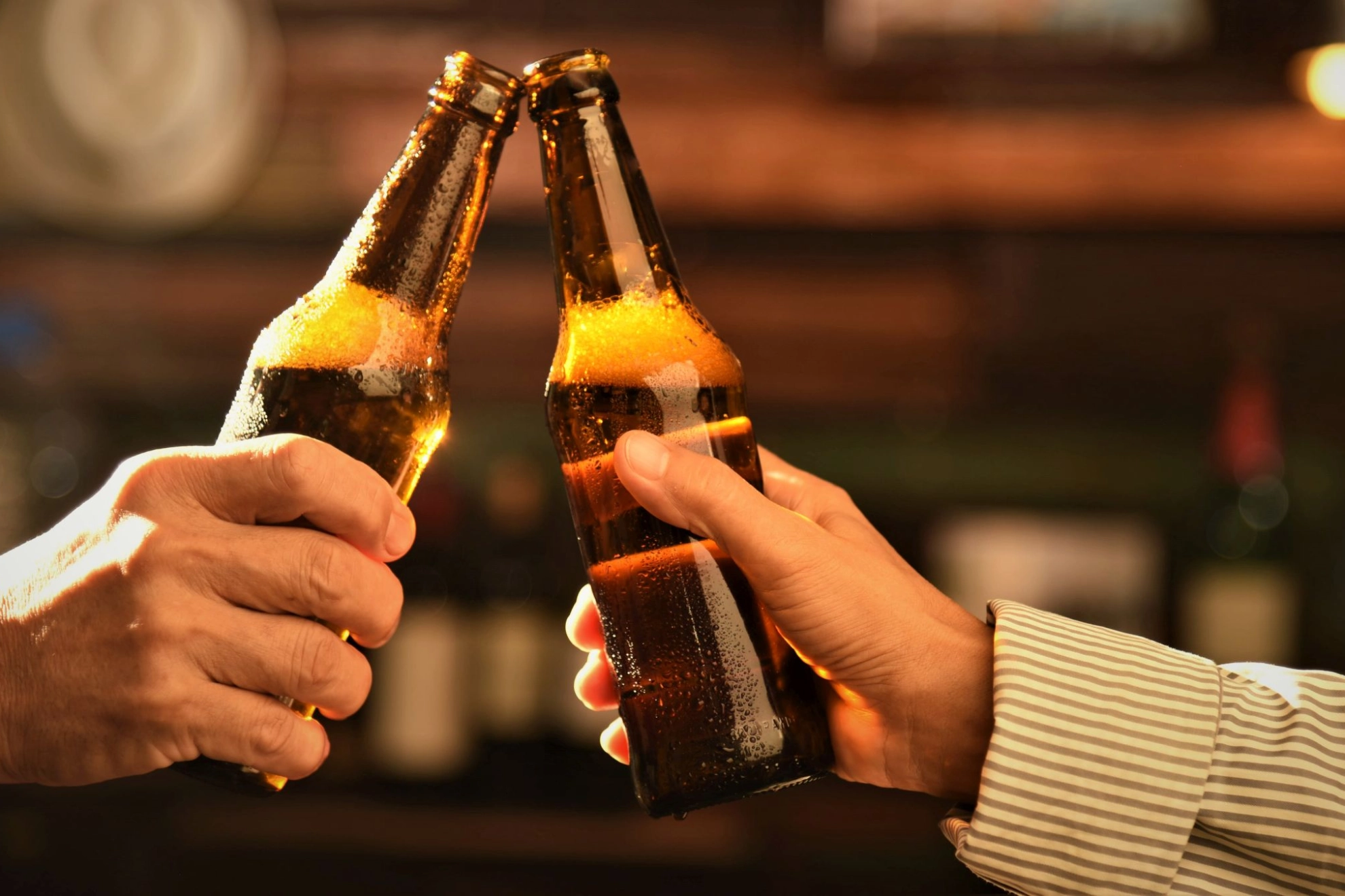 zwei Menschen stoßen mit zwei Flaschen Bier an